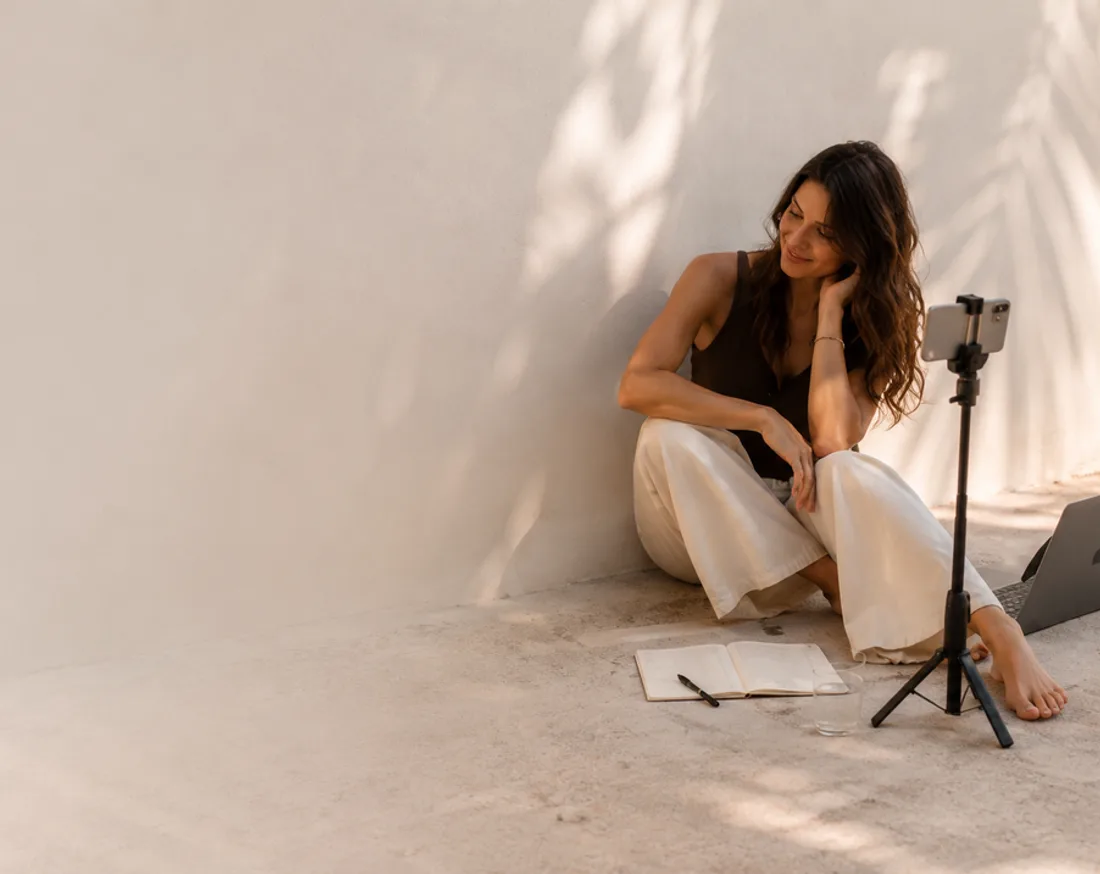 Mujer grabando contenido con el móvil y el portátil en el suelo